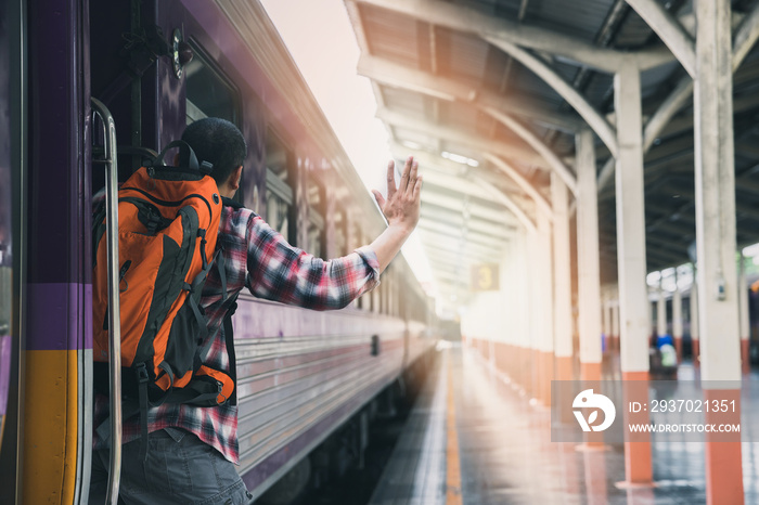 A man grabbed the handrail of the train door and waved his hand. People travel by local transport.