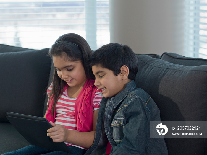 Children using tablet computer on sofa