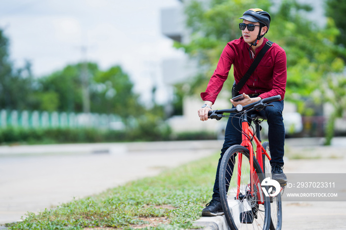 Asian man bicycles to work. He stops and uses his phone.