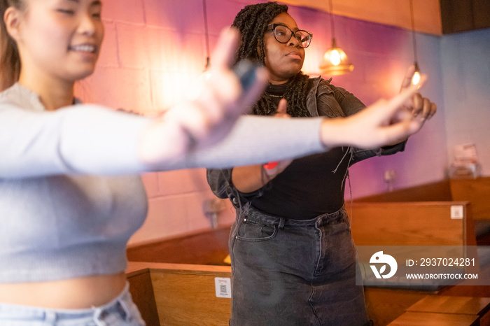 Female friends dancing while playing in video game at pub