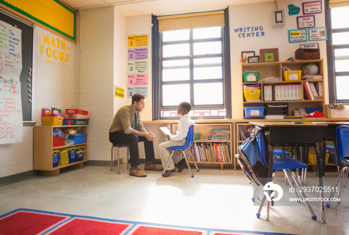 Male teacher and schoolboy (8-9) sitting face to face in classroom