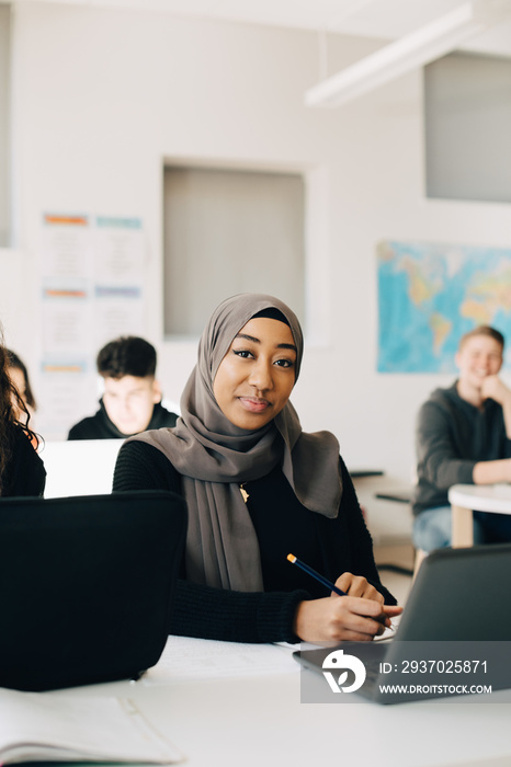 Portrait of smiling student using laptop while studying in classroom at high school