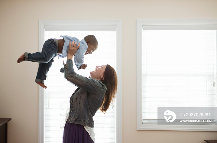 Side view of happy mother lifting her son at home