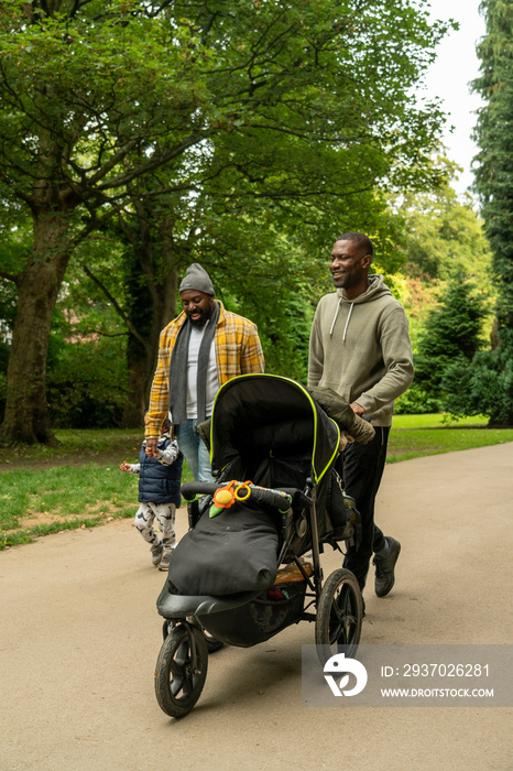 两名男子带着女儿和婴儿车在公园里散步