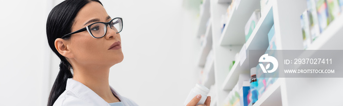 asian pharmacist in glasses looking at medication in drugstore, banner