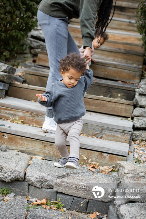 Black mother helping biracial son down the stairs in backyard in fall