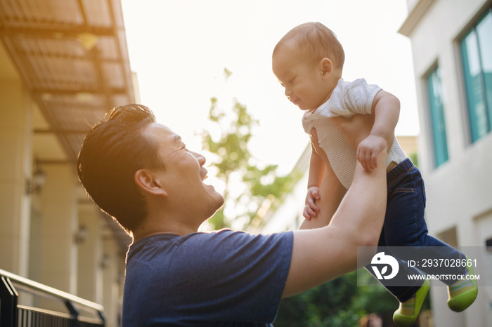 Happy Asian man holding his son to the air