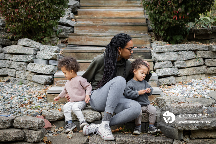 Black mom sitting with toddler twins on steps in backyard in fall