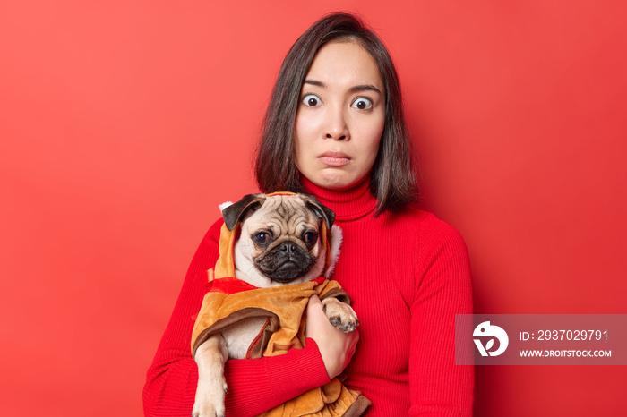 惊讶的女模特带着一只穿着保暖衣服的哈巴狗在户外散步