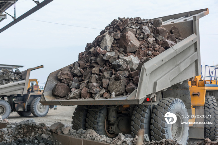 Mining industry: heavy dump trucks unload granite into huge rock crusher