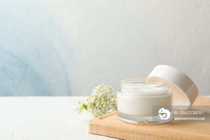 Jar with cream, allium flowers and board on white background, copy space