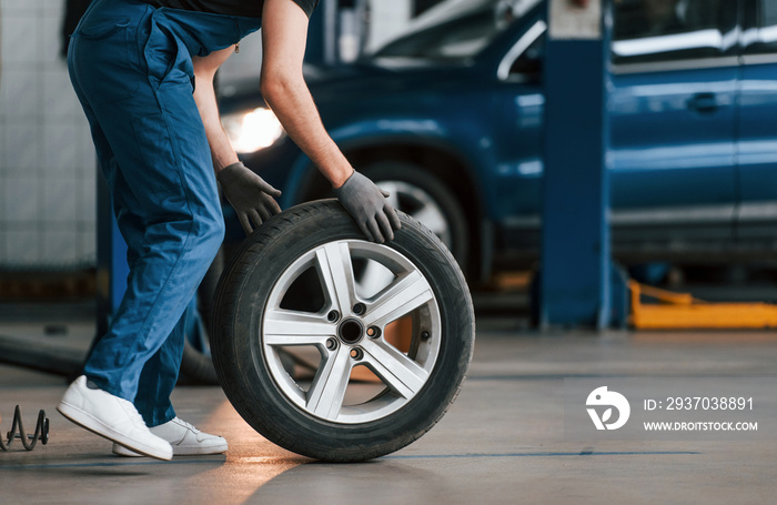 Close up view of man in work uniform with car wheel indoors. Conception of automobile service