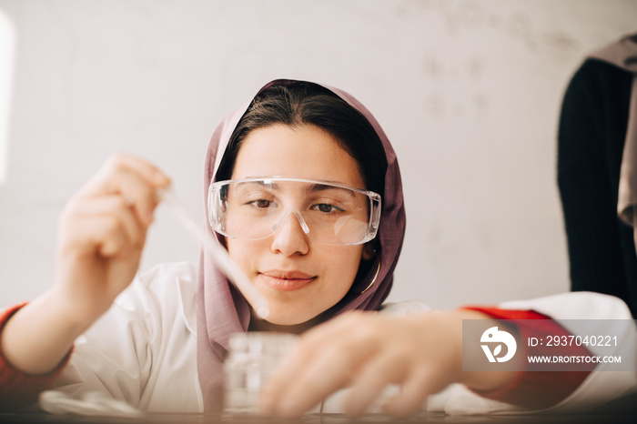 Close-up of teenage girl wearing hijab doing scientific experiment during chemistry class at univers