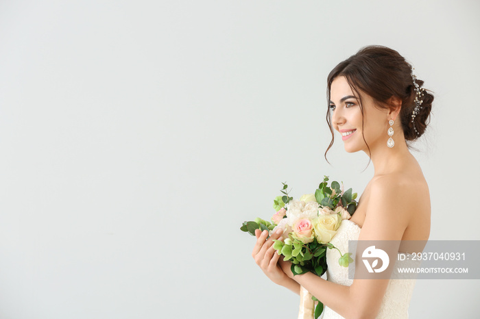 Beautiful young bride with bouquet of flowers on light background