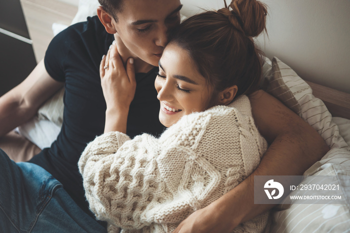 Caucasian man kissing his cute wife dressed in a white knitted sweater embracing in bed