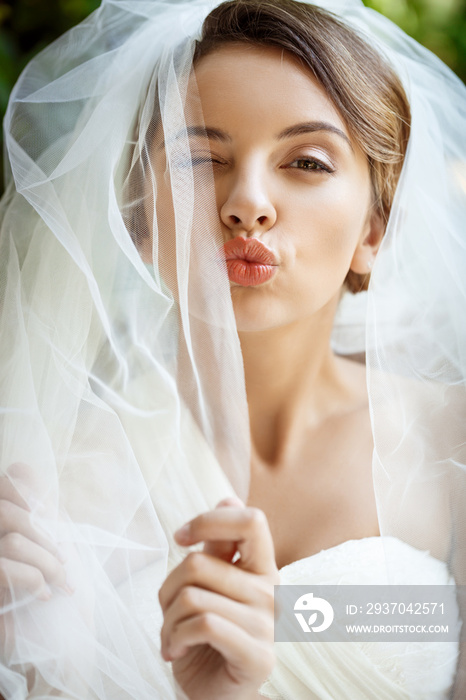 美丽的新娘穿着婚纱，戴着面纱眨眼，送上亲吻。