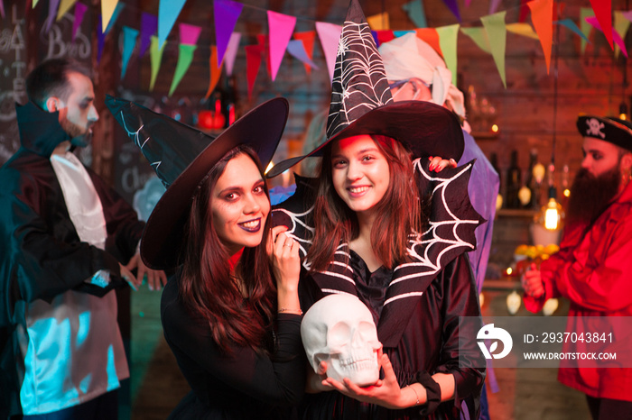 Beautiful young witch holding a human skull and smiling to the camera at halloween party