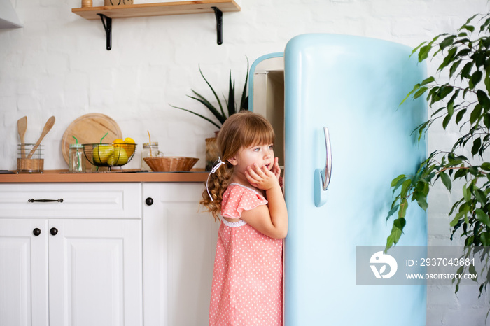 A little girl opens the door of the refrigerator. Beautiful kitchen.