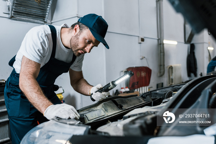 selective focus of bearded auto mechanic holding flashlight near car