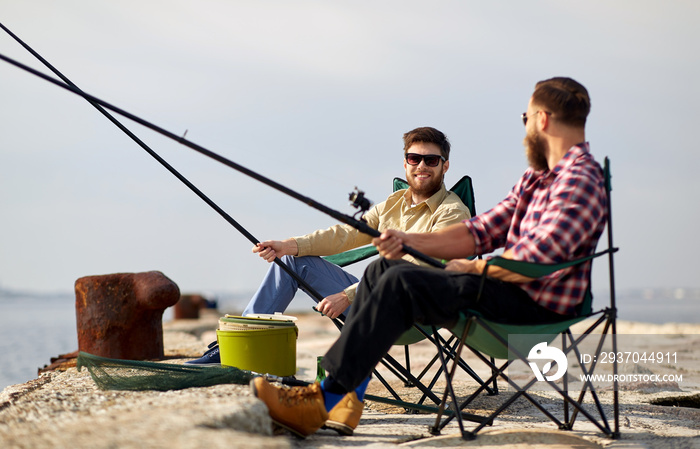 leisure and people concept - happy friends with fishing rods on pier at sea