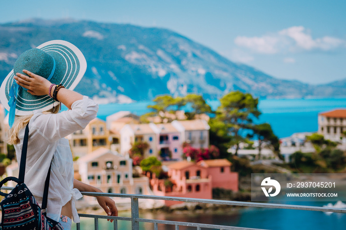 Tourist woman wearing blue sunhat and white clothes enjoying view of colorful tranquil village Assos