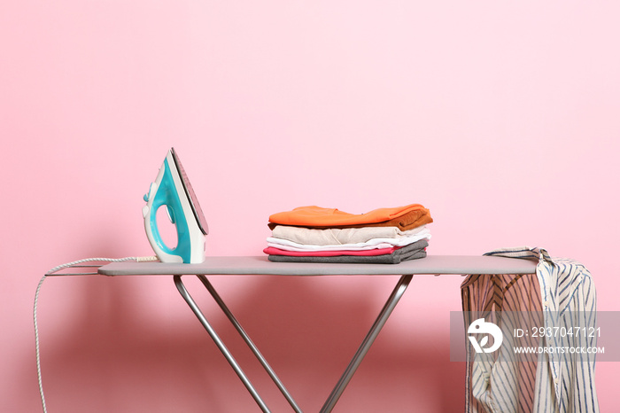 Iron and shirt on an ironing board on a colored background.