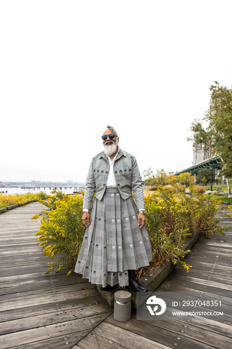 smiling man with gray hair and beard wearing skirt suit in waterfront natural area