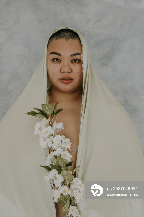 close up headshot of a plus size woman with a shaved head wearing a satin veil holding white flowers