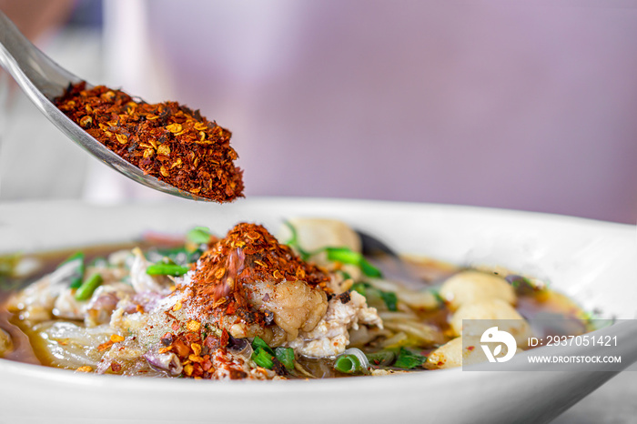 Asian woman hand pouring chili powder on noodle bowl , unhealthy eating spicy food concept backgroun