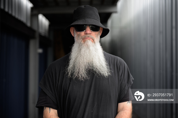 Mature handsome bearded hipster man wearing hat and sunglasses outdoors