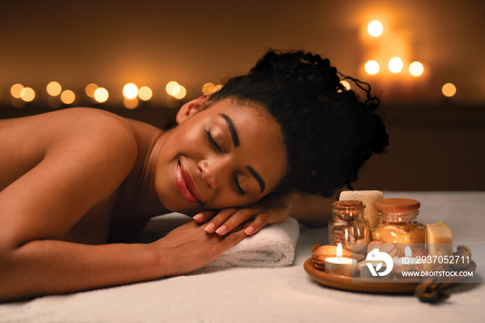 Smiling african woman lying on massage table at spa