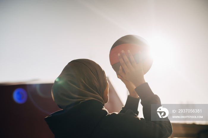 Teenage girl wearing hijab playing with ball on sunny day