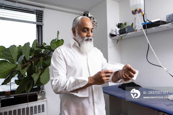 gray hair bearded man getting dressed in white shirt