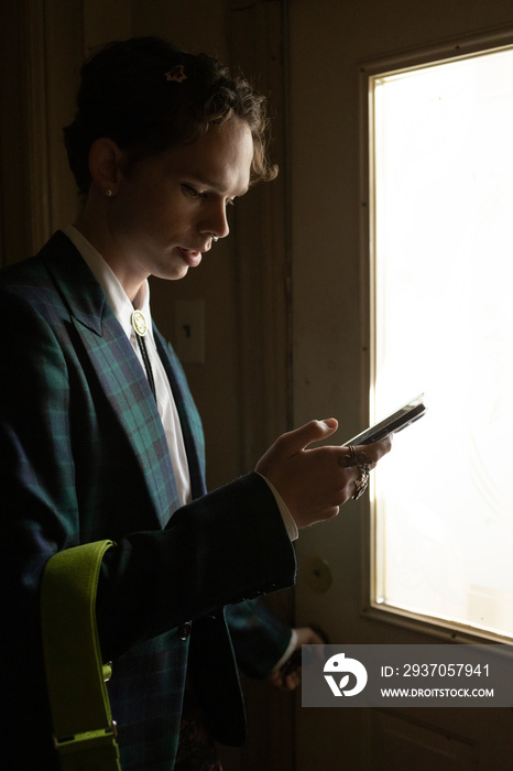 fashionable non-binary person in doorway looking at smartphone