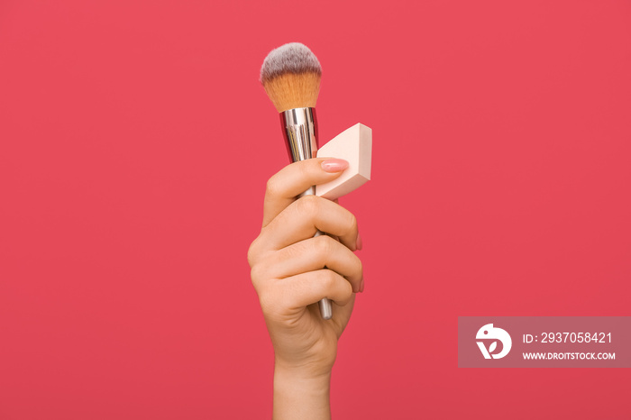 Female hand with stylish makeup sponge and brush on color background