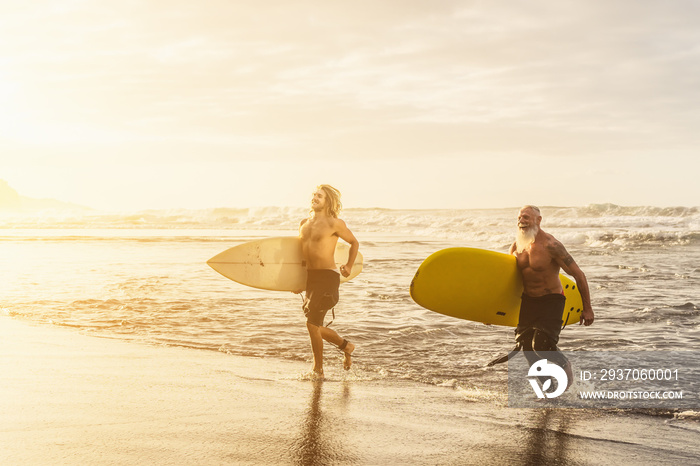 Happy friends with different age surfing together on tropical ocean - Sporty people having fun durin