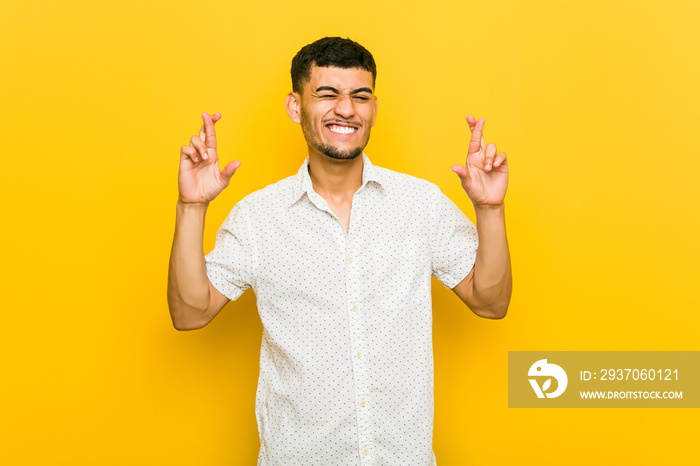 Young hispanic man crossing fingers for having luck