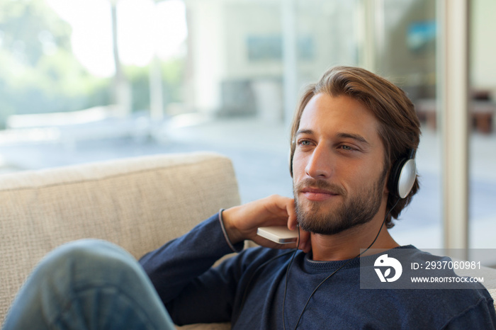 Serene young man listening to music with headphones on sofa