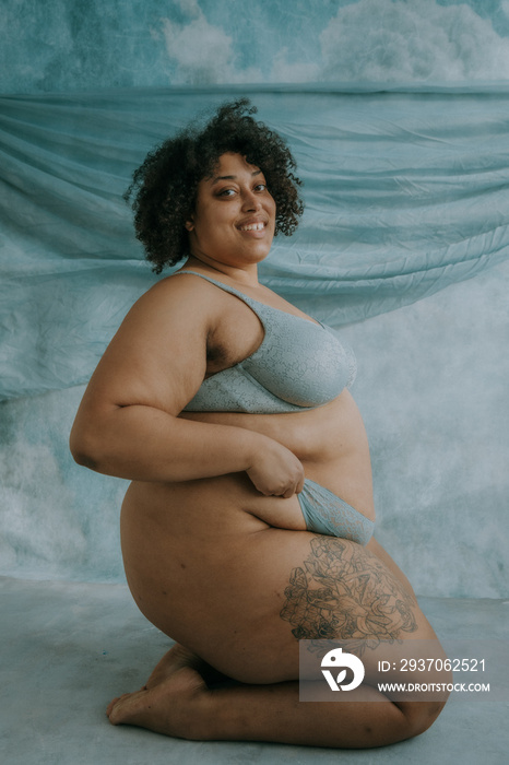 portrait of a plus size afro indigenous person sitting on knees wearing blue lignerie