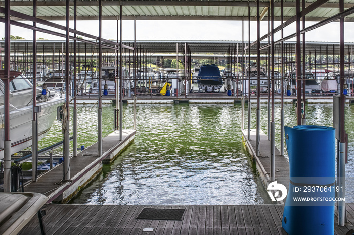 Empty boat slip in luxury boat dock at lake with other speedboats moored in distance - some up on ra