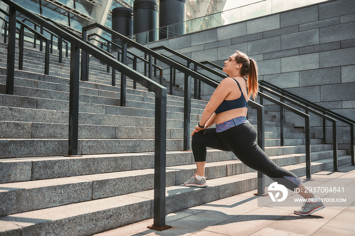 Stretching after great workout. Happy plus size woman in sport clothes doing stretching exercises on