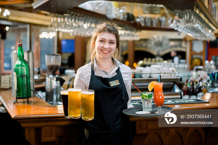 Smiling friendly waitress serving a pint of draft beer in a pub. Portrait of happy young woman servi