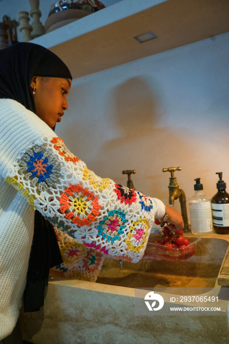 Woman wearing hijab washing cherry tomatoes in kitchen sink