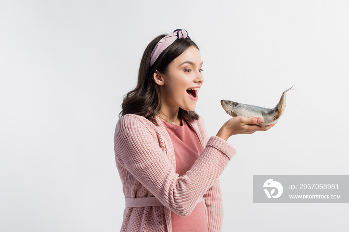 excited pregnant woman with open mouth holding dried fish isolated on white