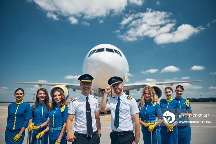 Cheerful airline workers standing in airfield under blue sky