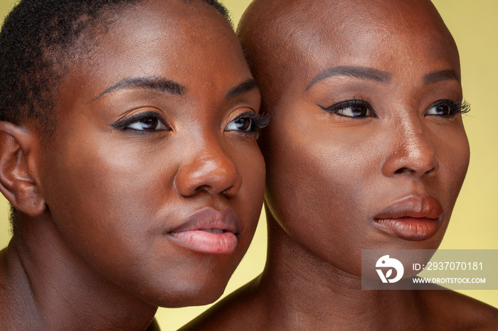 Studio portrait of two women cheek to cheek against yellow background