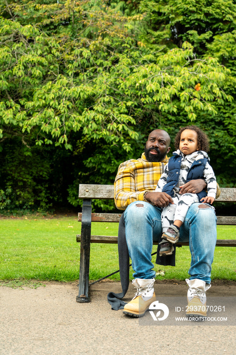 一名男子抱着女儿坐在公园的长椅上