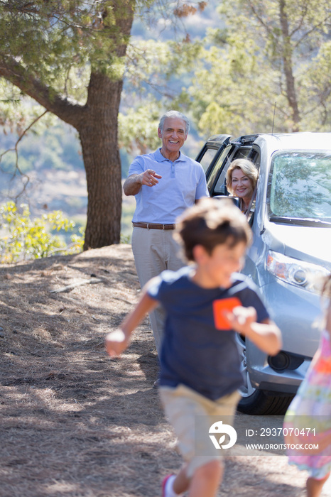 Playful grandparents and grandkids outside car at roadside