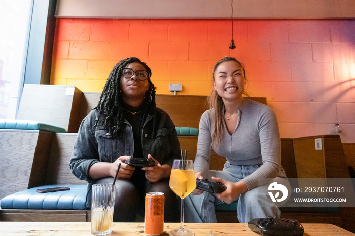 Female friends having fun while playing in video games at pub