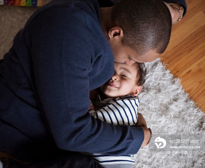 Father embracing son while relaxing on rug at home